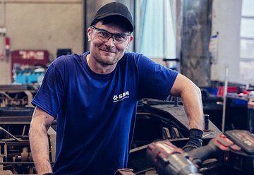 Werksarbeiter mit blauem Tshirt und Schutzbrille lächelt in Kamera